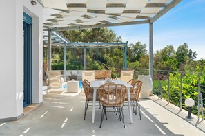 Une terrasse extérieure avec une table et des chaises, une piscine et une vue sur les arbres et la verdure.