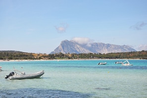 A coastal scene with clear turquoise waters, boats, and a mountain in the background. - Villa Asta (San Teodoro)