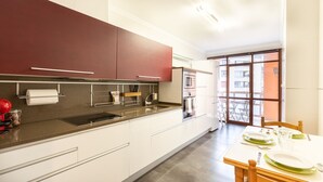 A modern kitchen with white and red cabinets, stainless steel appliances, and a dining area with a table set for two. - Txurruka - baskeyrentals (Mutriku)