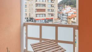 A balcony with a wooden table and chairs, overlooking a residential area with buildings and a hill in the background. - Txurruka - baskeyrentals (Mutriku)