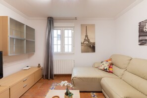 Un salon comprenant un canapé, un téléviseur, une fenêtre avec des rideaux, un radiateur et un tableau représentant la Tour Eiffel.