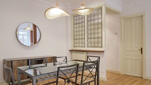 A dining area with a glass table and metal chairs, a round mirror, and two wicker pendant lights. - Catedral | The Rentals Collection (San Sebastián)