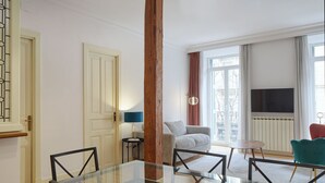 A modern living room with a glass dining table, a sofa, a TV, and a window with curtains. - Catedral | The Rentals Collection (San Sebastián)