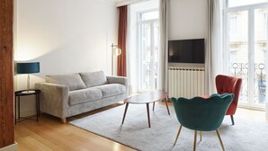 A modern living room with a sofa, a round coffee table, a teal armchair, and a TV mounted on the wall. - Catedral | The Rentals Collection (San Sebastián)