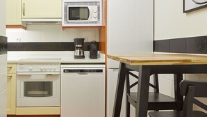 A compact kitchen with a microwave, stove, and dishwasher, a wooden table, and a chair. - Catedral | The Rentals Collection (San Sebastián)