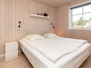 Un dormitorio con cama, mesitas de noche, una ventana y paredes de madera.