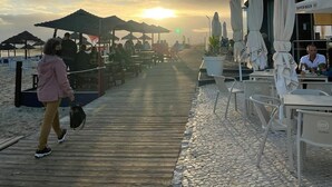 Ein Holzsteg führt zu Sitzgelegenheiten am Strand mit Sonnenschirmen mit Blick aufs Meer.