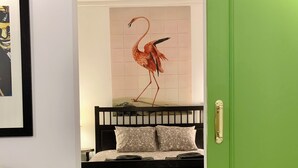 Ein Zimmer mit einer grünen Tür, einem schwarzen Bett mit gemusterten Kissen, einem Holztisch und einem Wandbild mit einem roten Vogel.