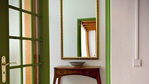 Eine grüne Tür mit Fenster, ein Holztischchen mit Schale und ein Spiegel an der Wand.