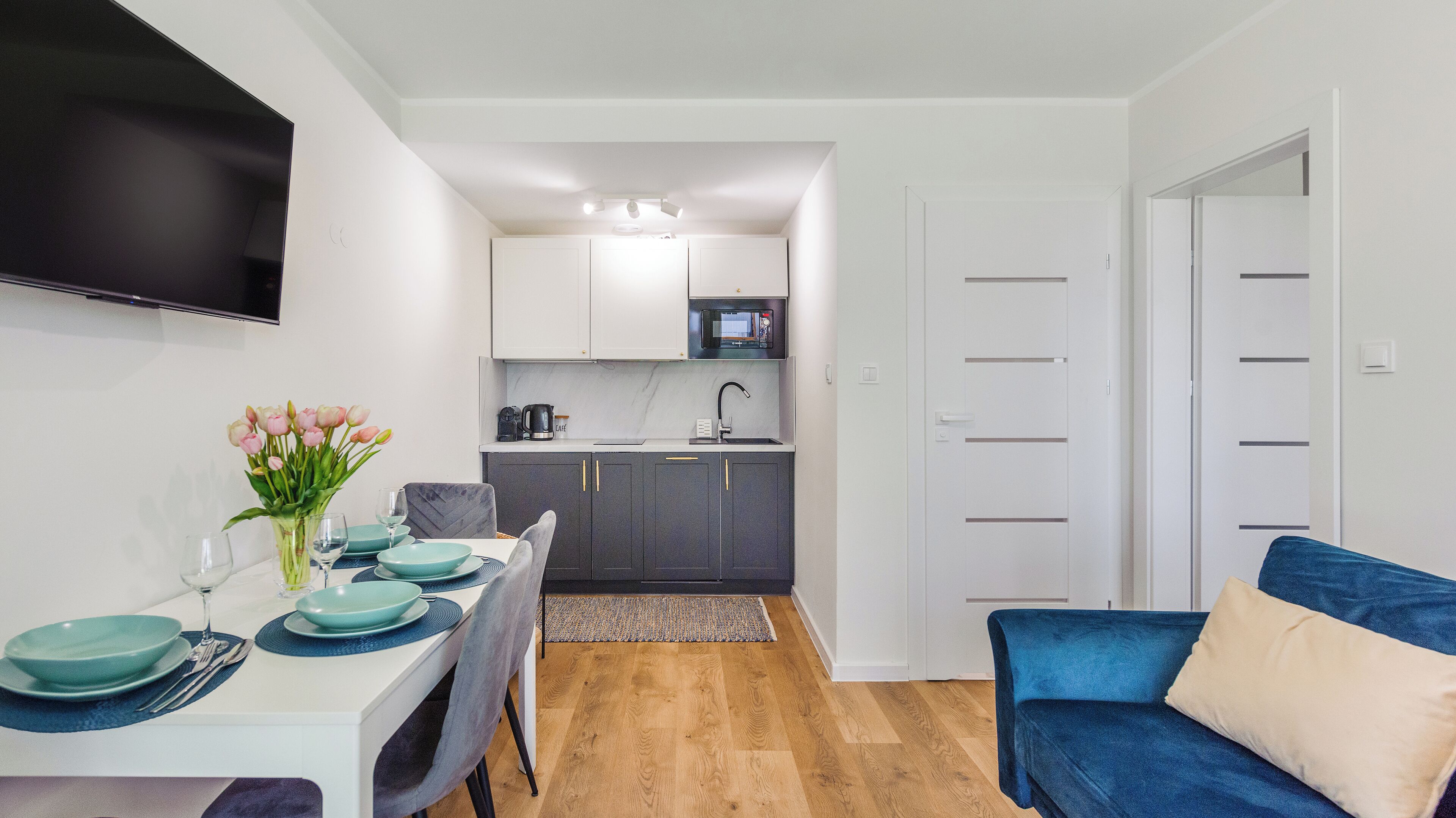 Un espace de vie compact comprenant un coin repas, une kitchenette et un canapé bleu.