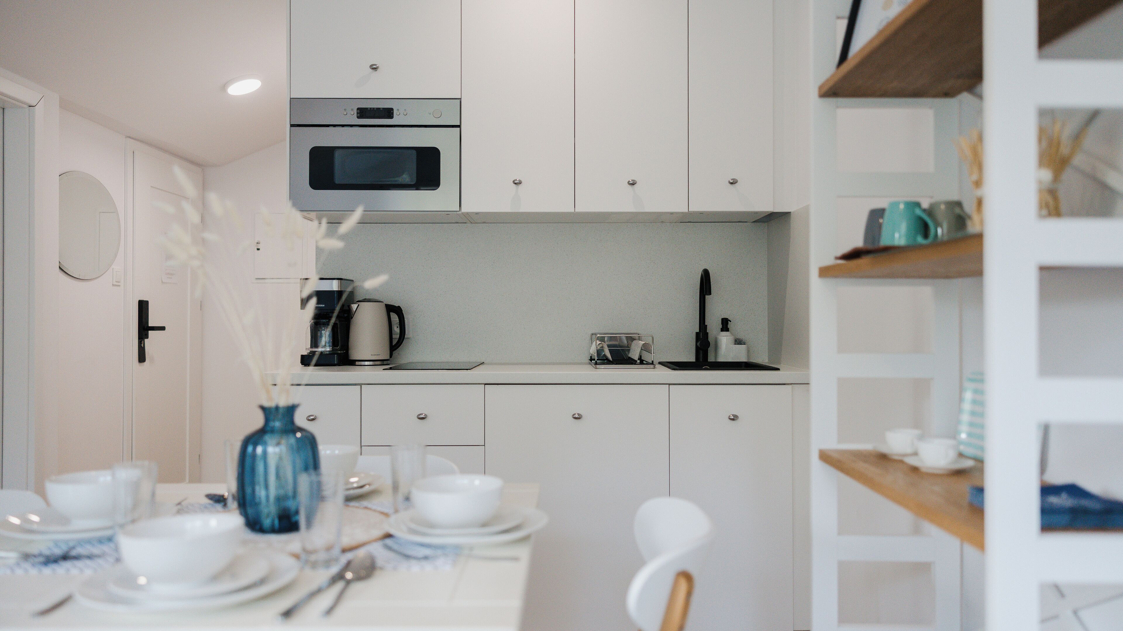 A compact kitchen with white cabinets, a microwave, a coffee maker, and a sink.