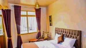 Una habitación de hotel con cama, una silla, una mesita y ventana con cortinas.