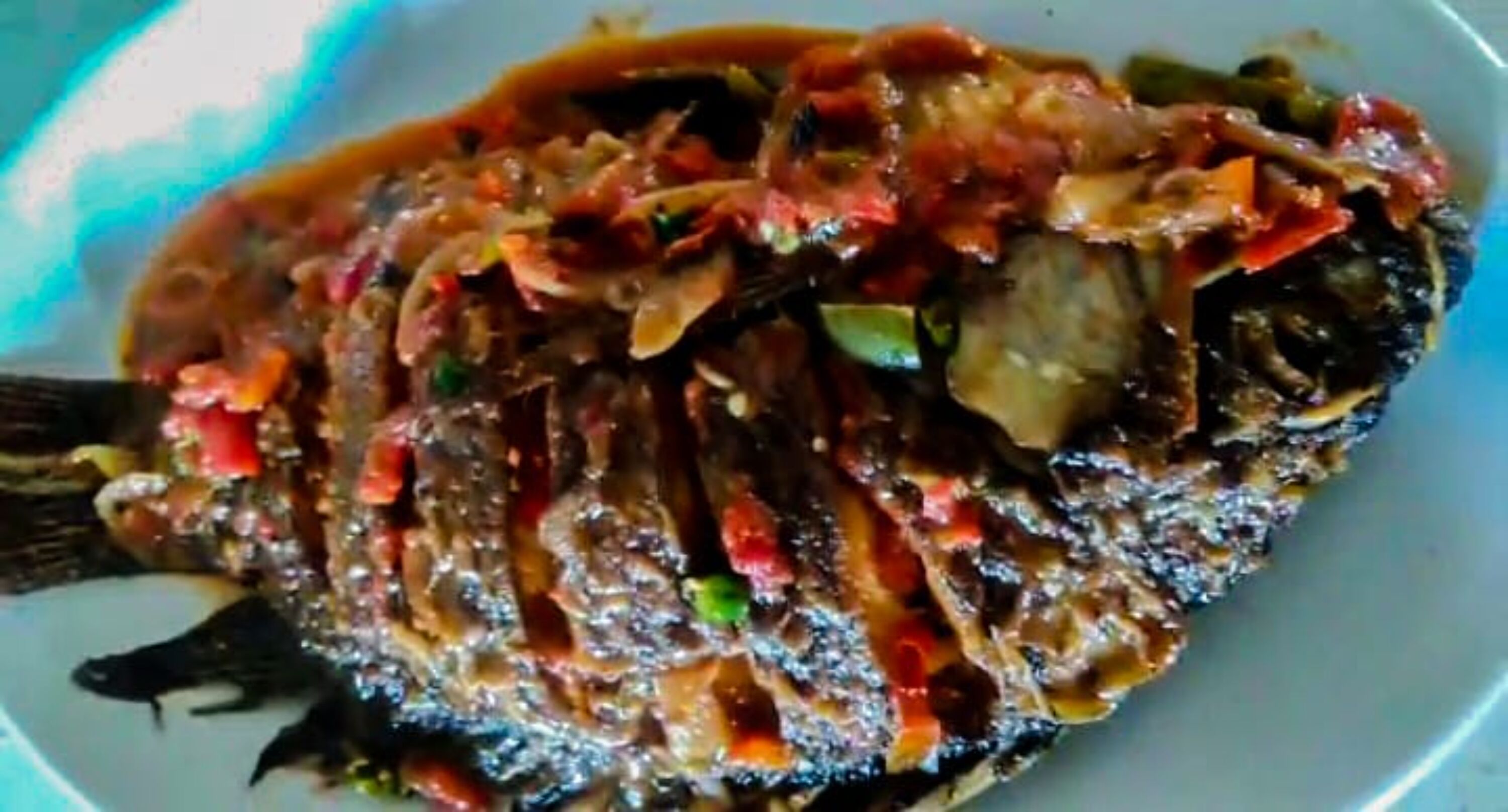 Un plato de pescado con salsa oscura y brillante, y verduras en rodajas.