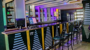 Una zona de bar con mostrador, taburetes y estantes llenos de botellas.