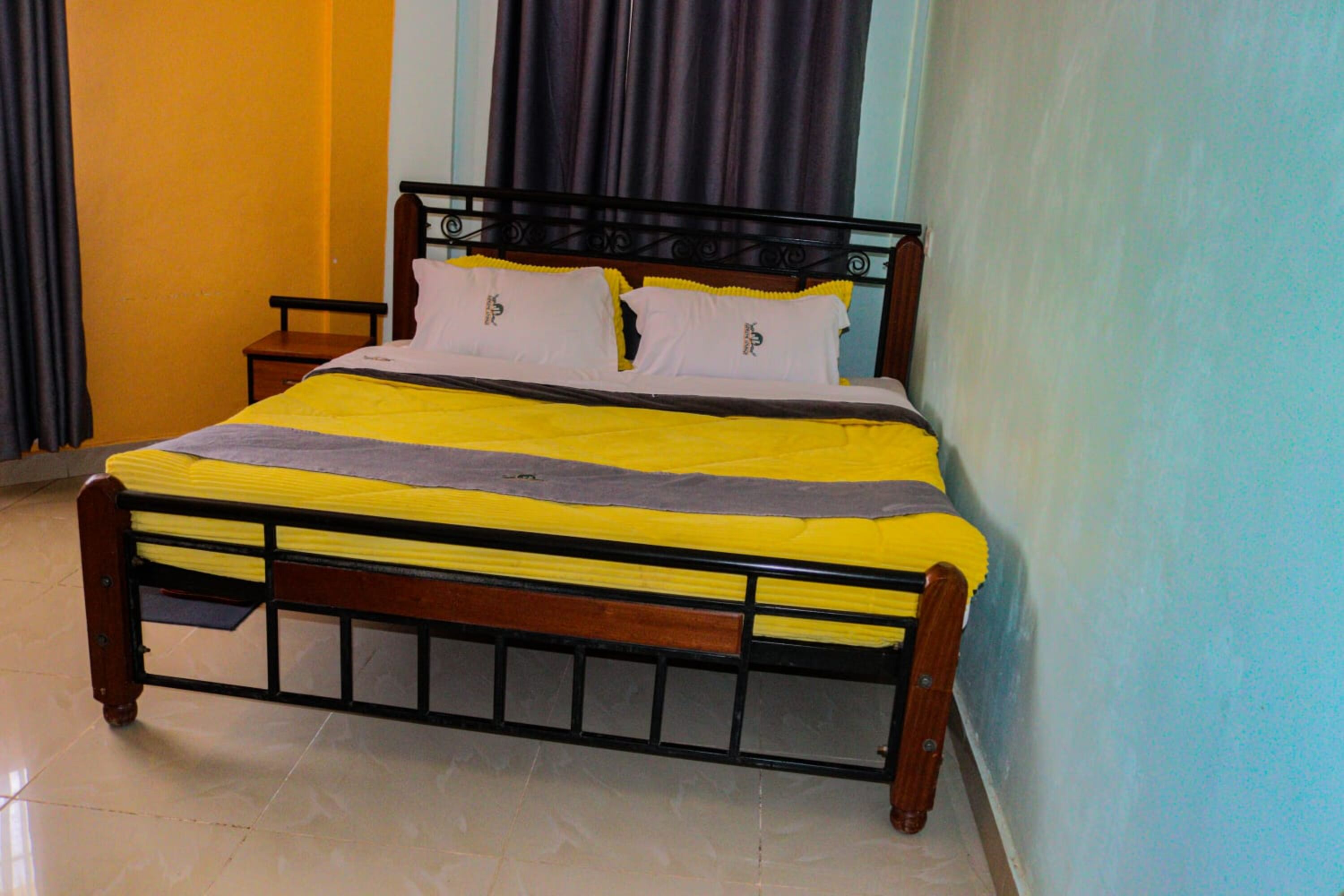 A bed with a metal frame, wooden headboard, and a yellow and gray bedspread.