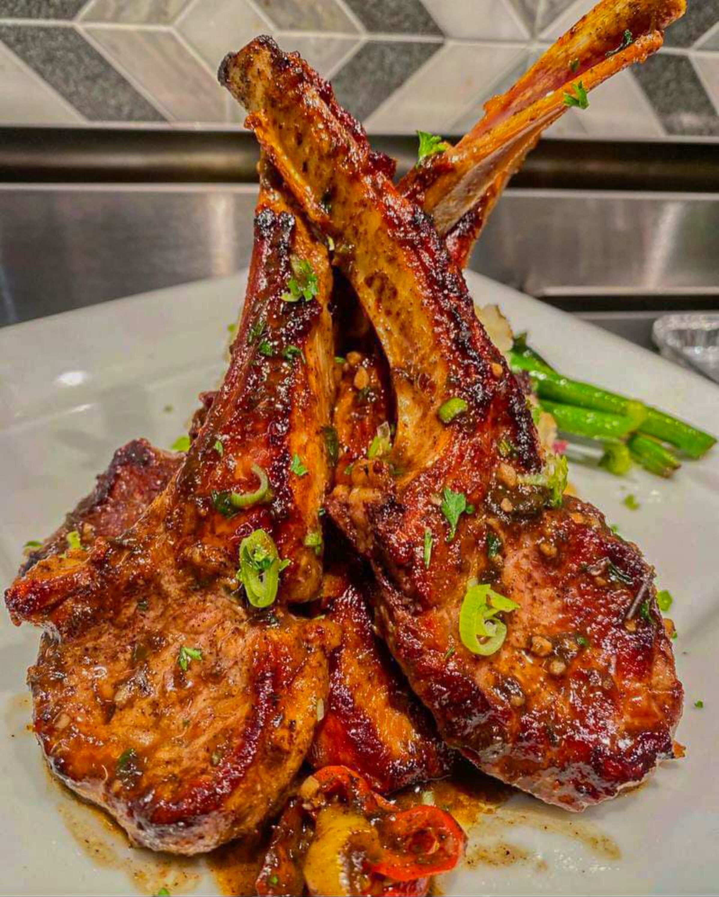 A plate of grilled lamb chops with a glaze, garnished with herbs.