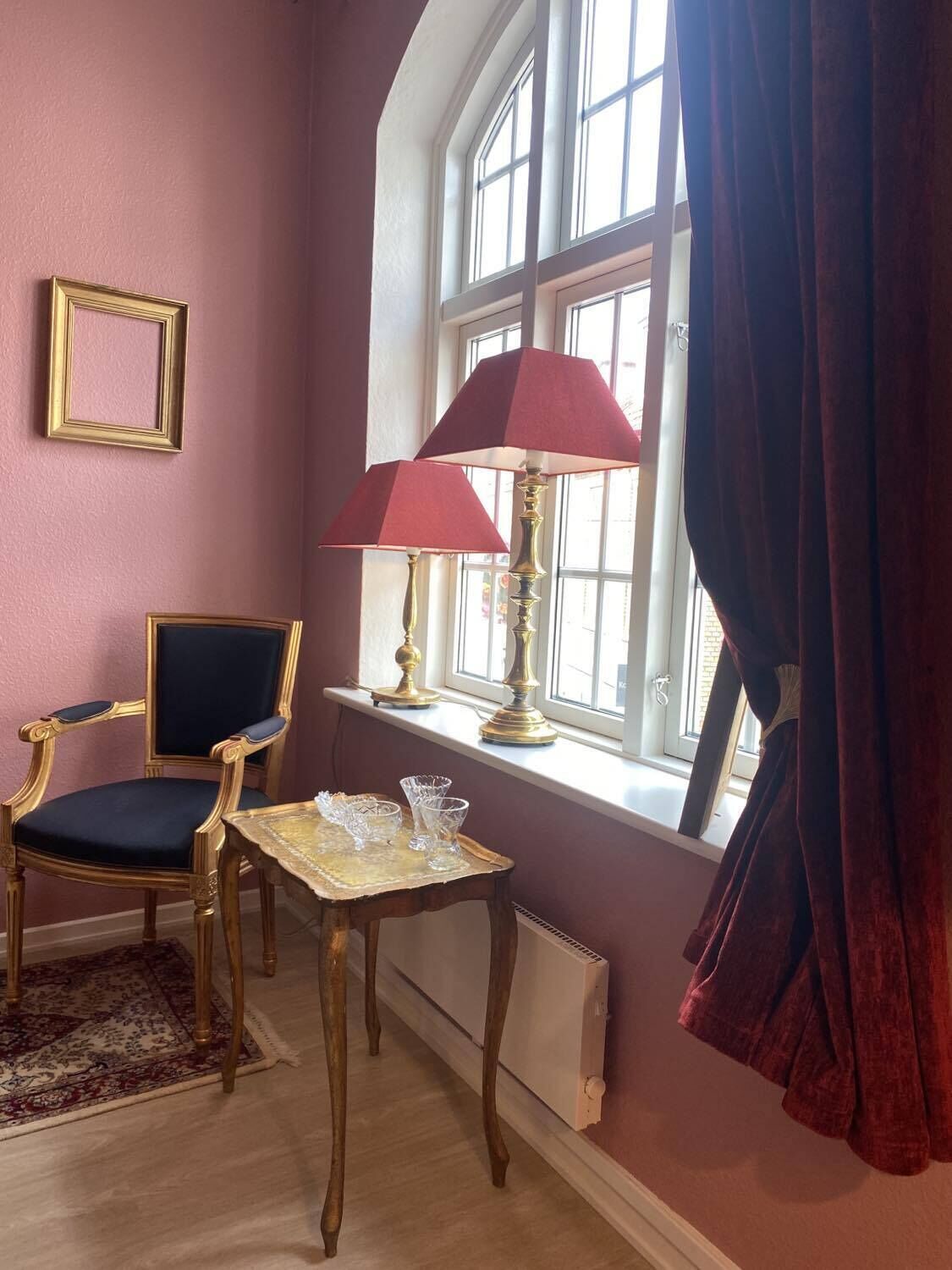 Una habitación con un ventanal grande, una silla, una mesa con vasos y una lámpara.