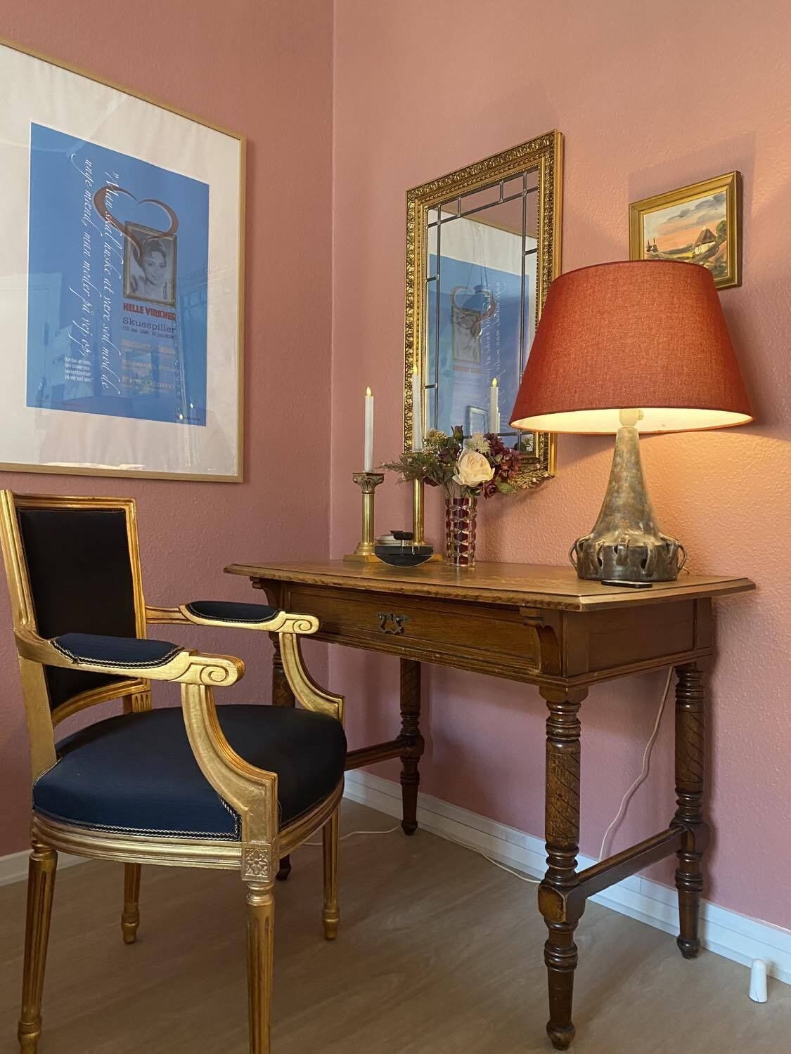 A room with a vintage-style desk, a chair, a mirror, and a wall-mounted lamp.