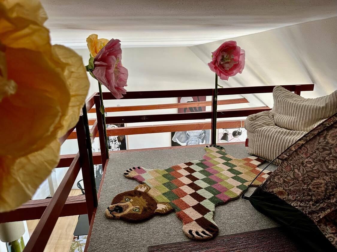 Quarto com varanda de madeira, tapete estampado e um brinquedo macio no chão.