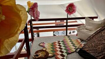 Quarto com varanda de madeira, tapete estampado e um brinquedo macio no chão.