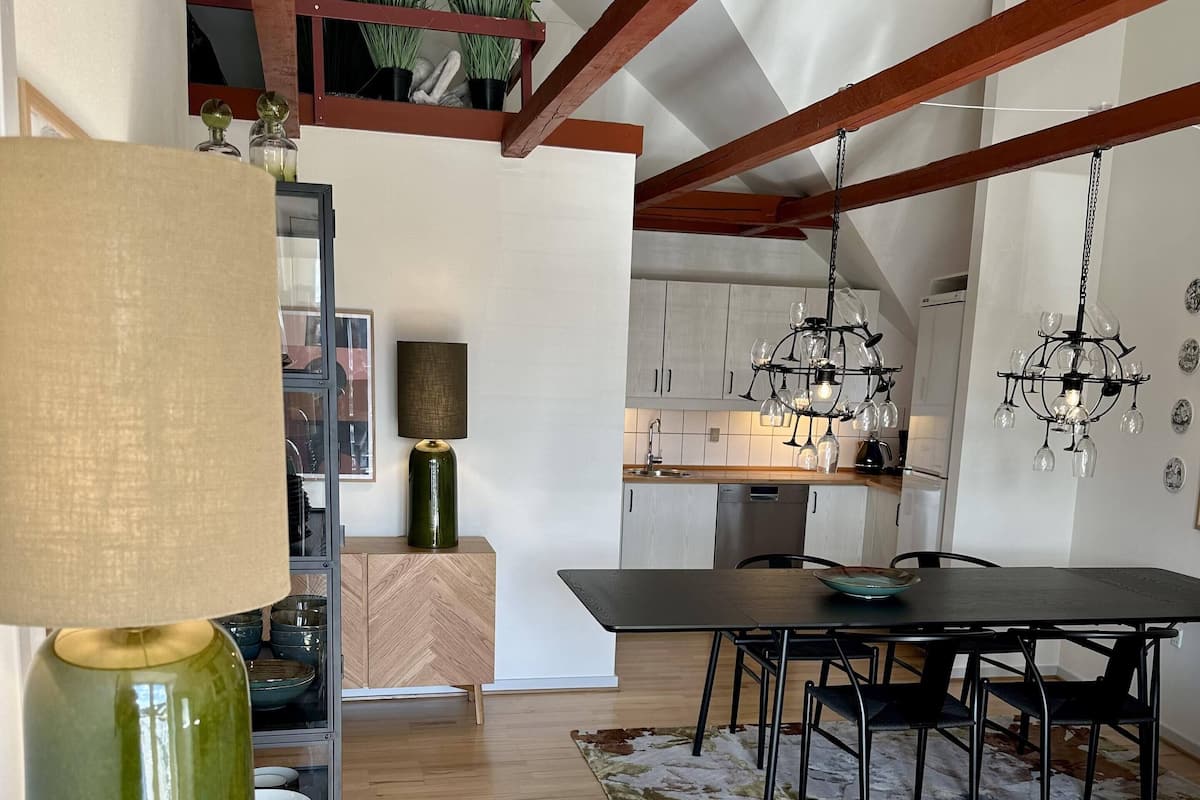 Une cuisine moderne avec des poutres en bois, un coin repas avec une table et des chaises, et un espace de vie avec un canapé et une lampe.