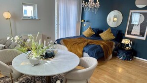 Una sala moderna con una mesa redonda, dos sillones, un sofá y una cama con cabecera azul.