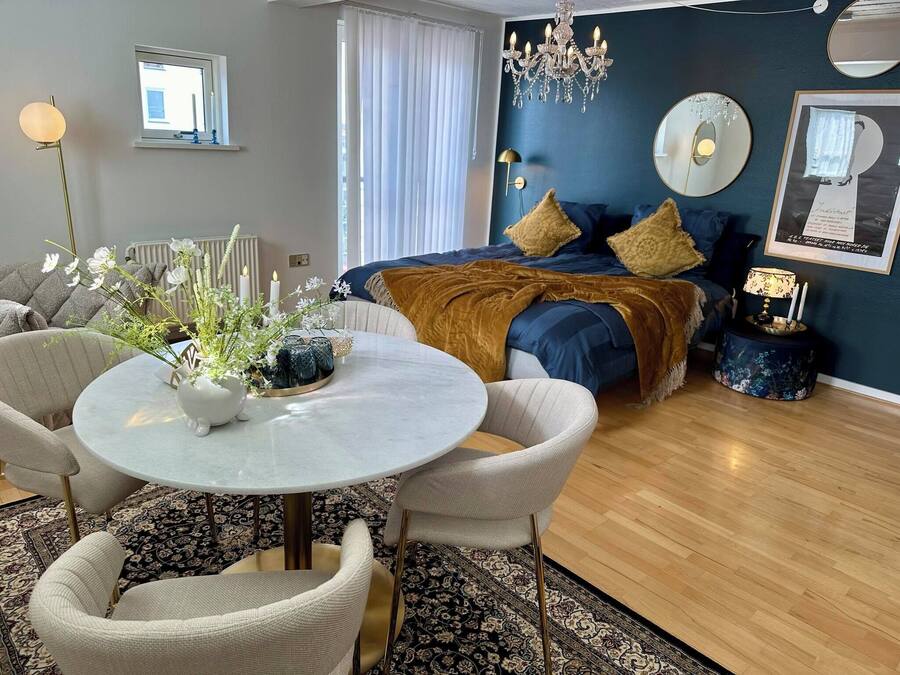 Una sala moderna con una mesa redonda, dos sillones, un sofá y una cama con cabecera azul.