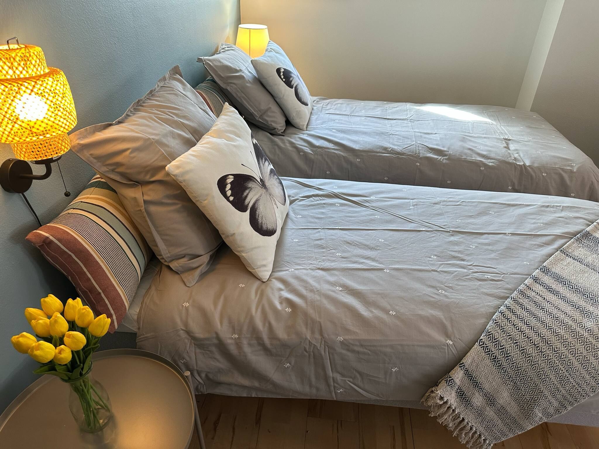A bedroom with two beds, a lamp, and a vase of yellow flowers.