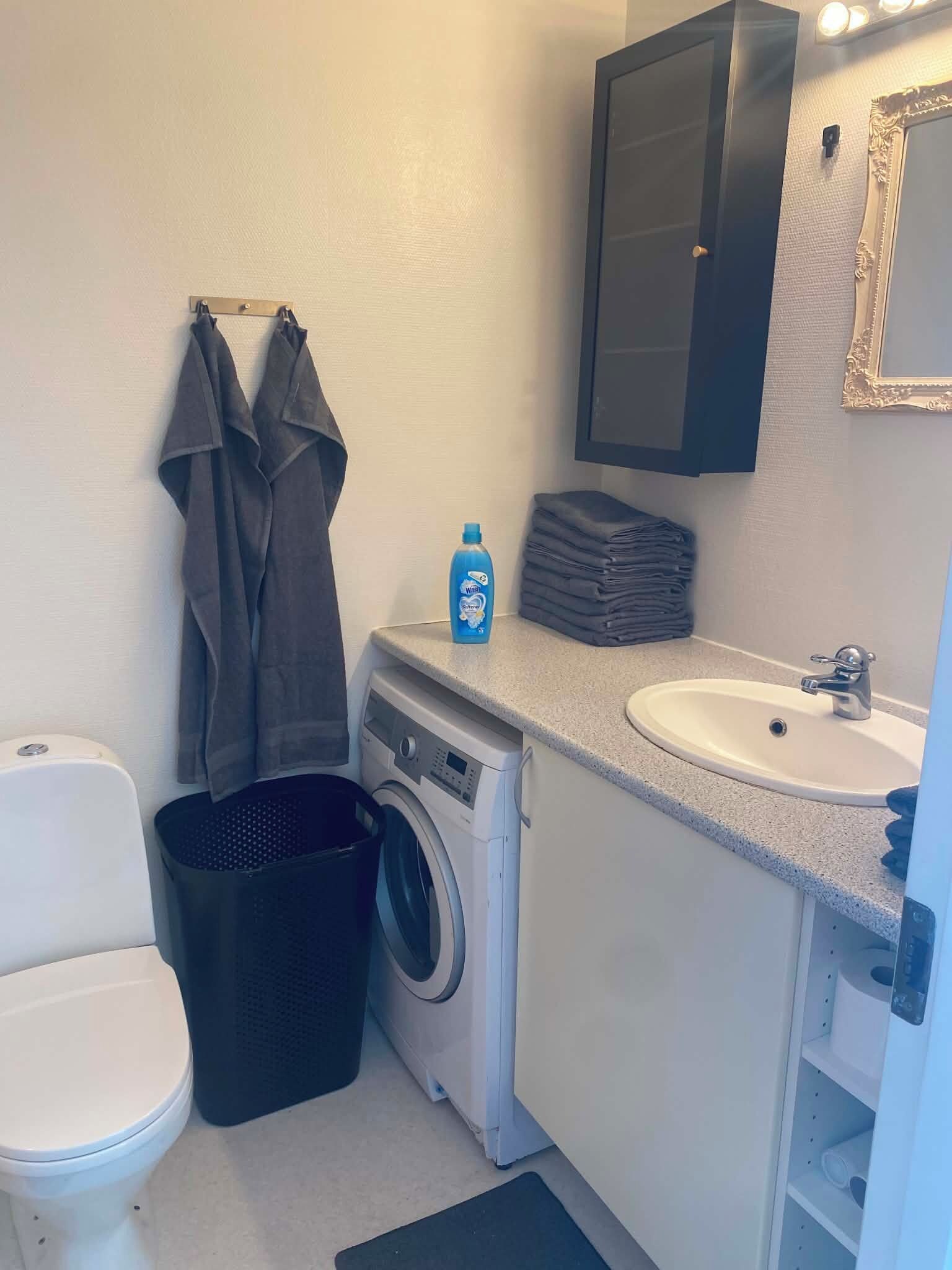 Un baño pequeño con lavadora, lavamanos, inodoro y espejo.