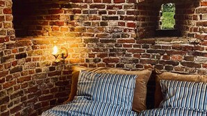 Una habitación con pared de ladrillo, una lámpara de pared encendida y una cama con ropa de cama a rayas.