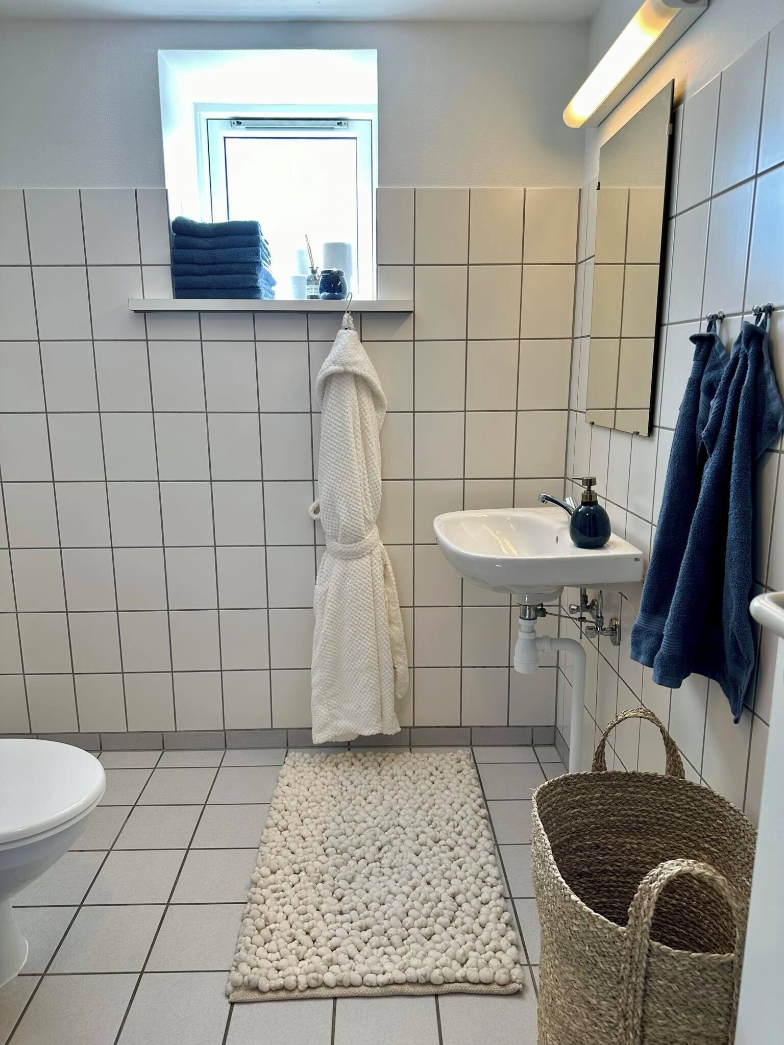 A bathroom with a white sink, a mirror, a window, and a white bath mat.