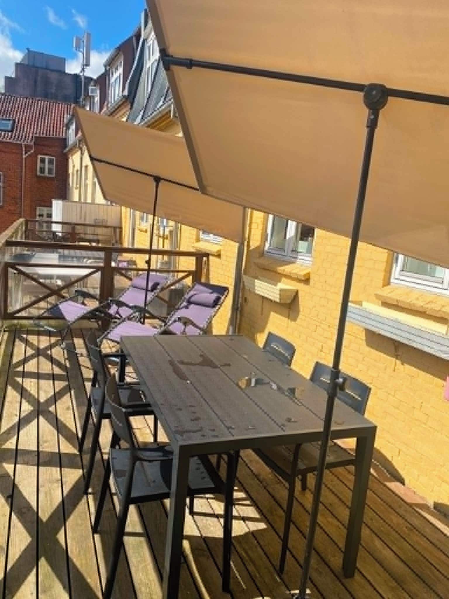 An outdoor deck with tables and chairs, covered by umbrellas, and a wooden floor.