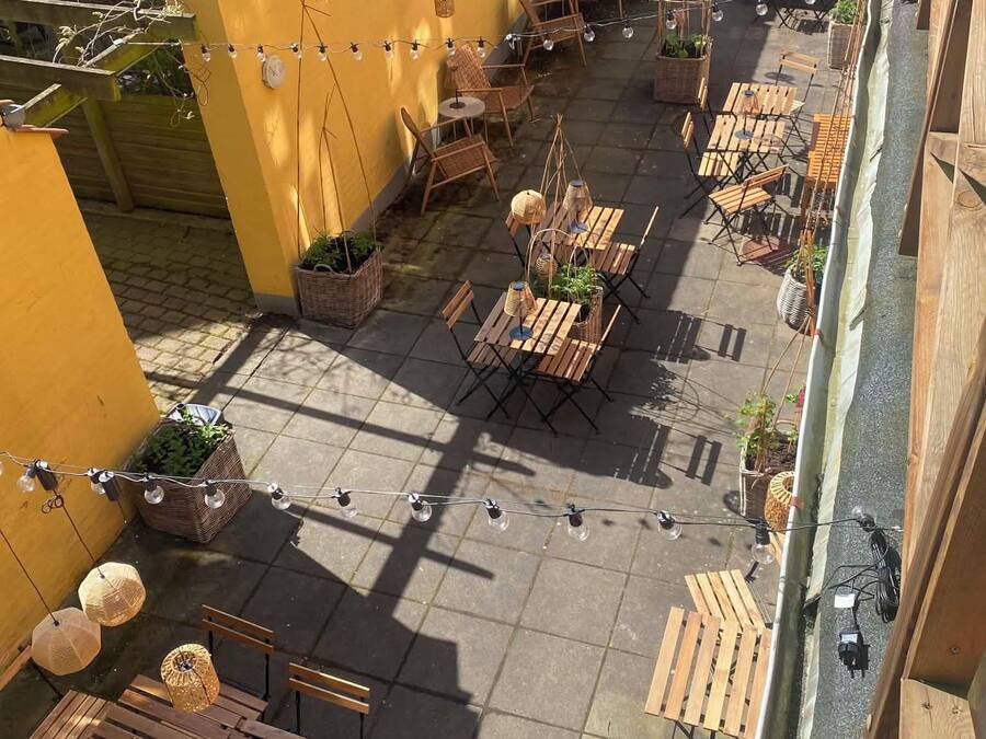 An outdoor patio area with multiple wooden tables and chairs, string lights, and potted plants.