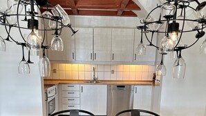 Una cocina moderna con armarios blancos, un comedor con mesa negra y una araña con copas de vino.