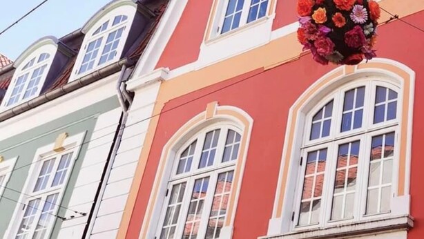Un edificio con fachada roja, marcos de ventana blancos y una maceta colgante con flores.