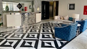 A modern hotel lobby with a geometric patterned floor, a reception desk, a sofa, and a chandelier. - Damac Tower studio in the center of Amman (عمّان)
