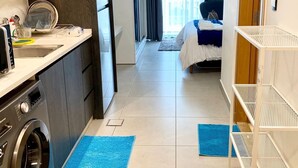 A compact hotel room with a kitchenette, a washing machine, a bed, and a view of the city through large windows. - Damac Tower studio in the center of Amman (عمّان)