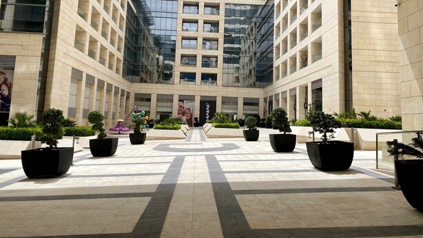 A modern building with a glass facade and a central courtyard with potted plants and seating areas. - Damac Tower studio in the center of Amman (عمّان)
