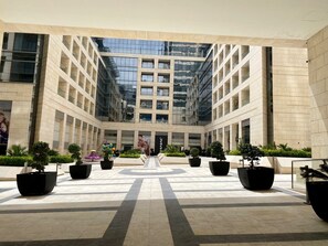 A modern building with a glass facade and a central courtyard with potted plants and seating areas.