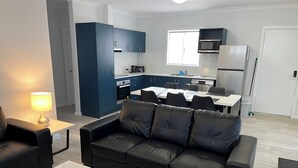 Una sala de estar moderna con un sofá de cuero negro, una mesa de centro blanca y un comedor con una mesa y sillas blancas.