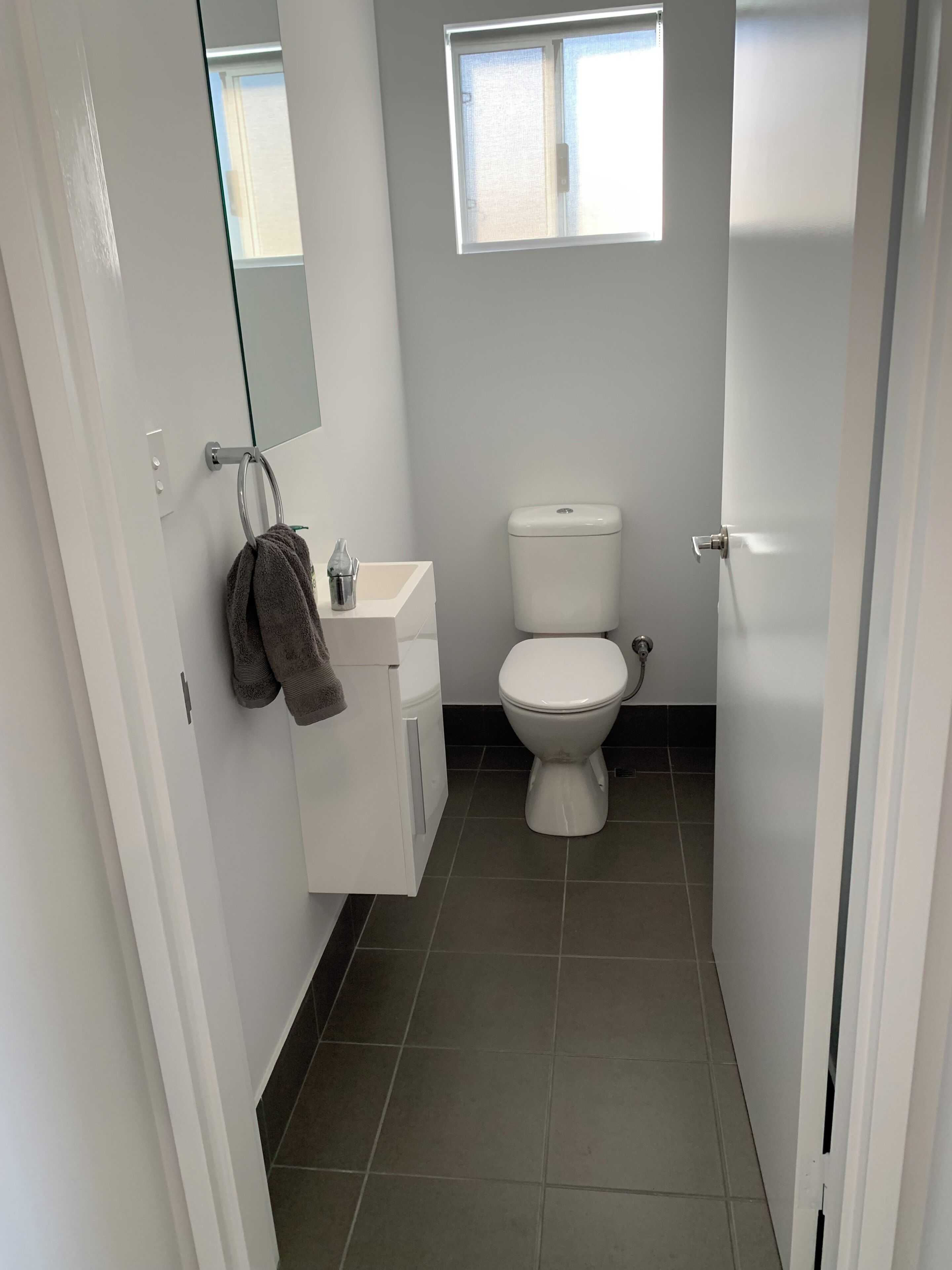 A bathroom with a toilet, a sink, a towel rack, a mirror, and a window.