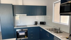 Una cocina moderna con armarios azules, horno integrado, cafetera, tostadora y lavavajillas.