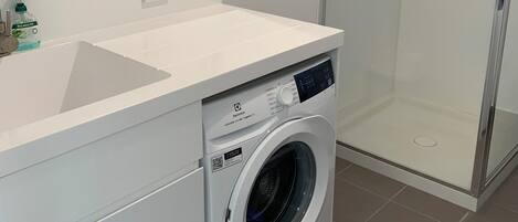 Ein modernes Badezimmer mit Waschmaschine, Duschkabine aus Glas und Spiegel.