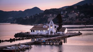 Une église blanche, dotée d’un clocher, se dresse sur une petite île au milieu d’une étendue d’eau calme. Elle est entourée d’un quai où sont amarrés des bateaux, et on aperçoit en arrière-plan une zone résidentielle.