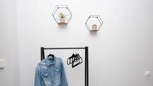 Une pièce dans laquelle on peut voir une veste en jean suspendue à un portant, deux étagères murales hexagonales ornées de plantes, et un cintre noir sur lequel sont accrochés des vêtements.