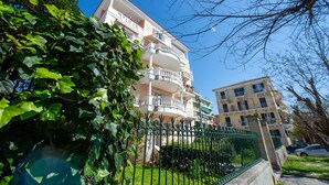 Un immeuble à plusieurs étages doté de balcons, entouré de verdure et d’une clôture.