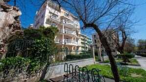 Un immeuble résidentiel à plusieurs étages, doté de balcons, entouré de verdure et délimité par un mur de pierre.