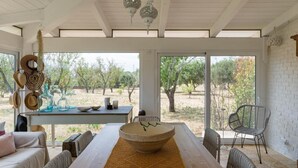 A spacious room with a large wooden table, a woven chair, and a view of a desert landscape through large windows. - Trullo Letizia con Piscina by Wonderful Italy (Ostuni)