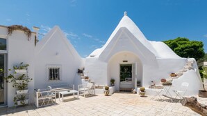 A white, modern building with a unique triangular roof design, outdoor seating area, and potted plants. - Trullo Letizia con Piscina by Wonderful Italy (Ostuni)