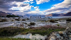 A remote, rustic building with a flat roof, surrounded by rocky terrain and a body of water. - Pangong Nest Cottage (Leh)